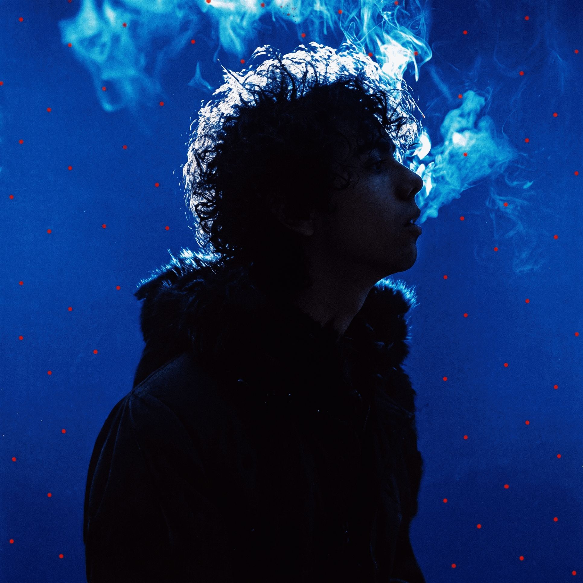 Steven Mendez de perfil sobre un fondo azul cobalto, con humo azul que sube, al estilo de la portada de Bocanada de Cerati
